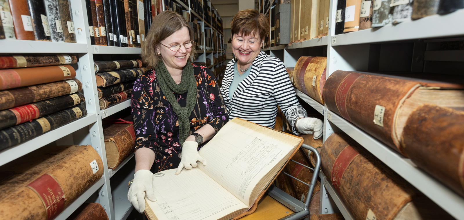 Hanne Hieta ja Hanna Lehto katselevat vanhaa kirkonkirjaa arkistossa