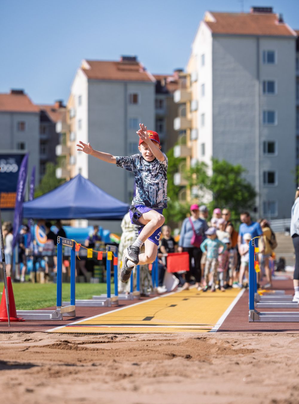 Lapsi hyppäämässä pituutta Paavo Nurmi -stadionilla. Taustalla muita lapsia vanhempineen.