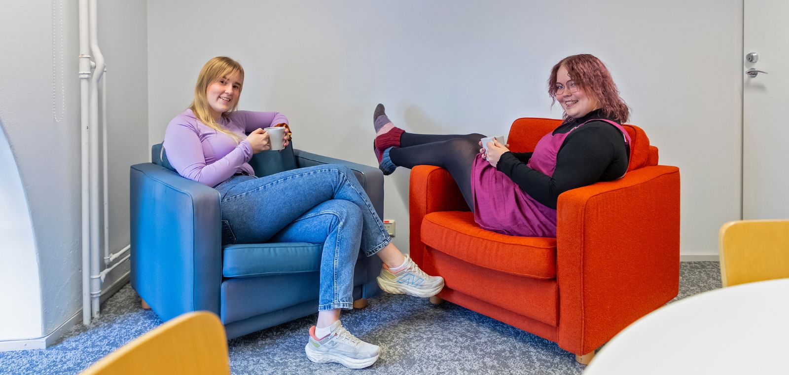 Kaksi nuorta naista istuu nojatuoleissa ja juo teetä.
