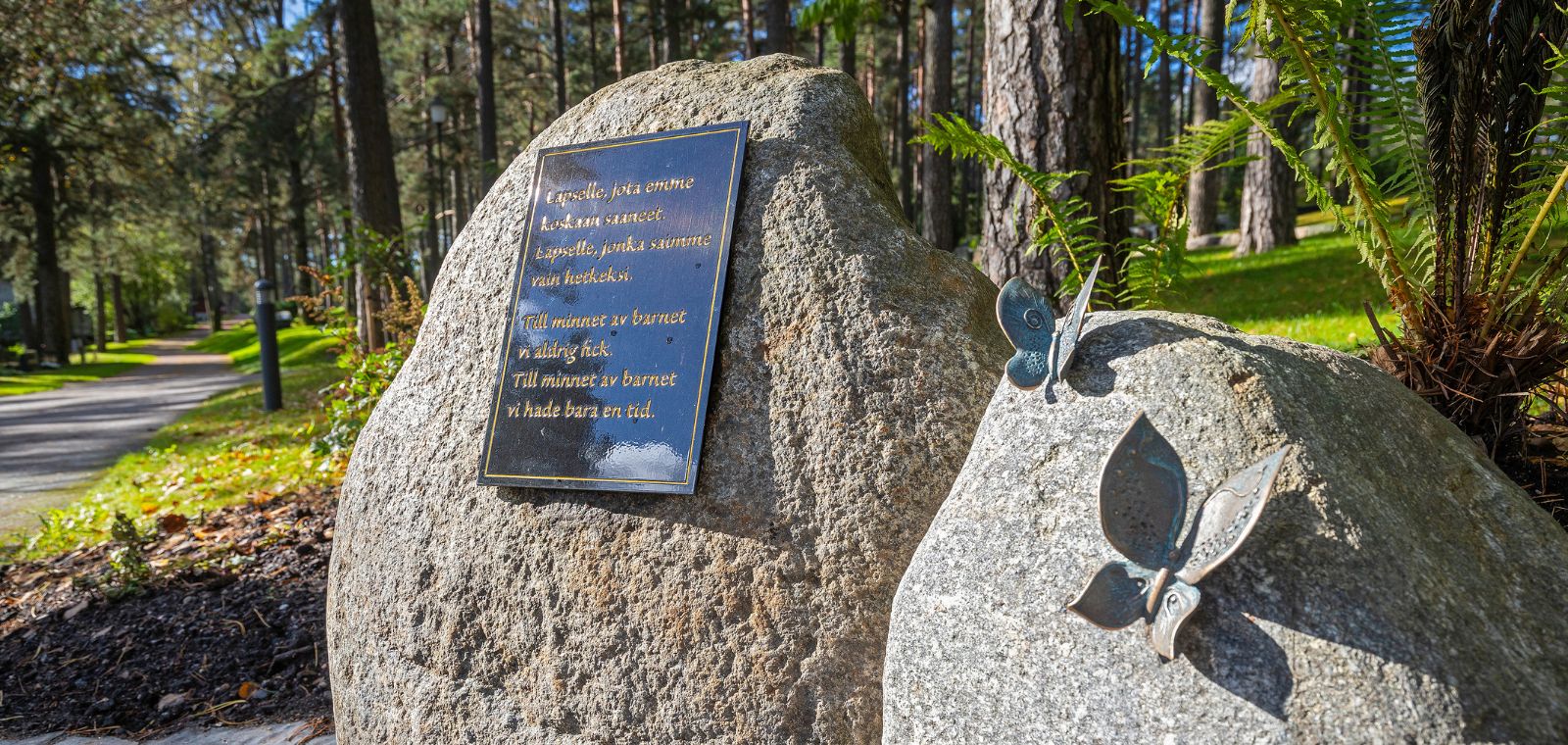 Kahdesta luonnonkivestä muodostuva muistomerkki. Toiseen kiveen on kiinnitetty metallilaatta, toiseen kaksi metallista tehtyä perhosta.