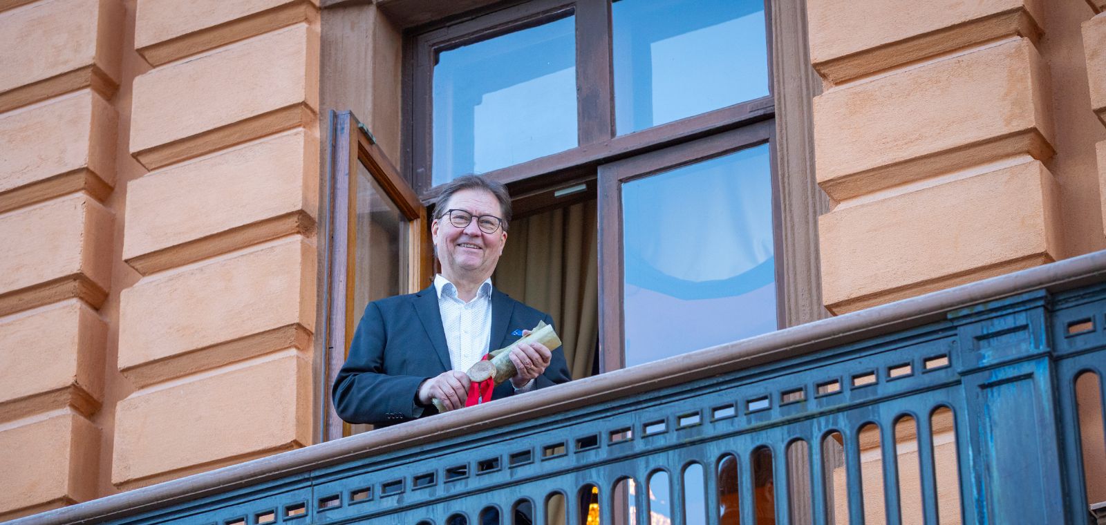 Parvekkeella seisova mies pitelee paperikääröä kädessään.