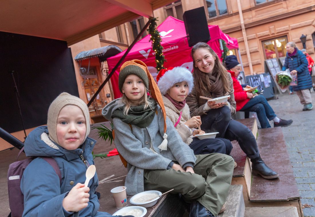 Kolme lasta ja nainen syövät riisipuuroa joulumarkkinoilla.