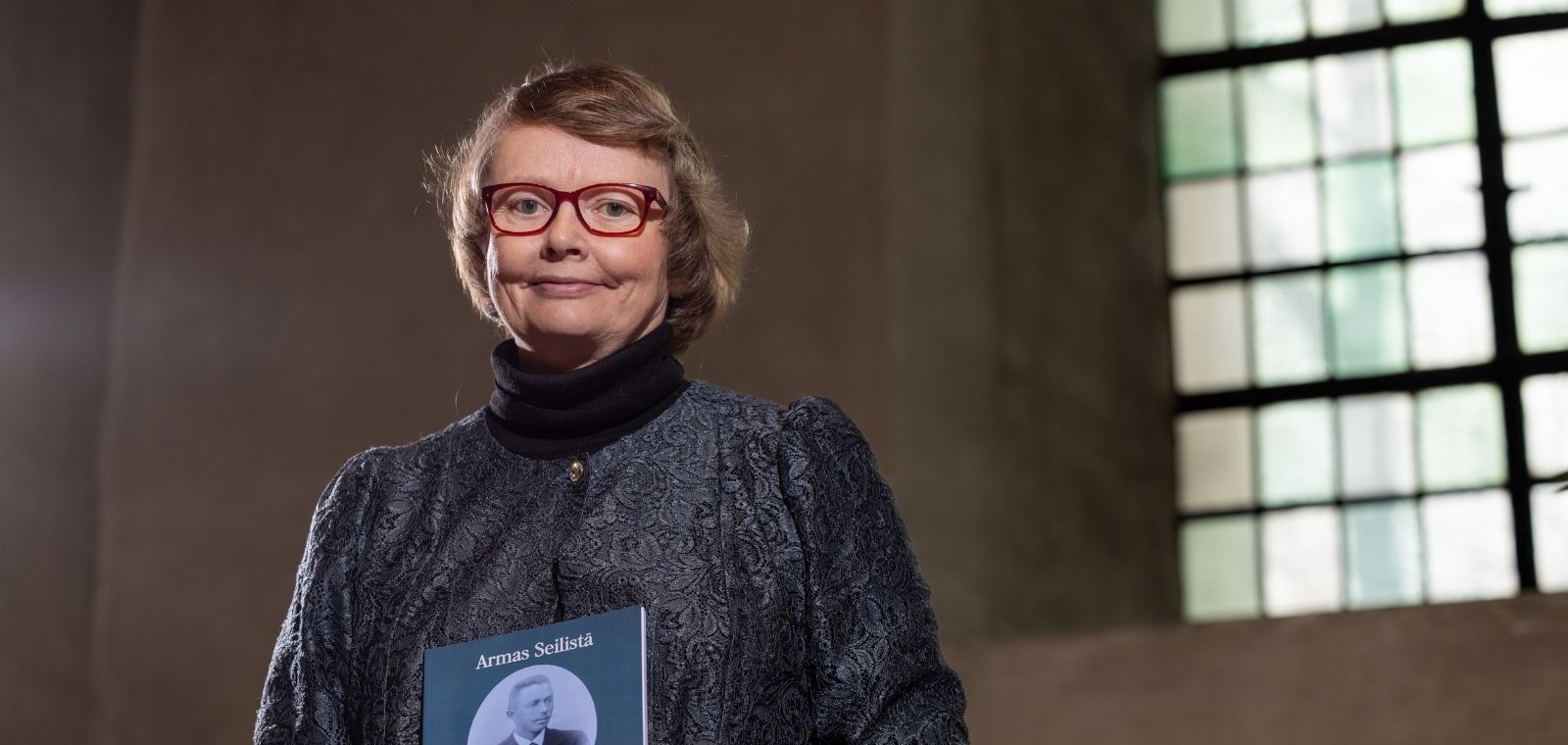 Nainen vanhassa kivirakennuksessa kädessään kirja.