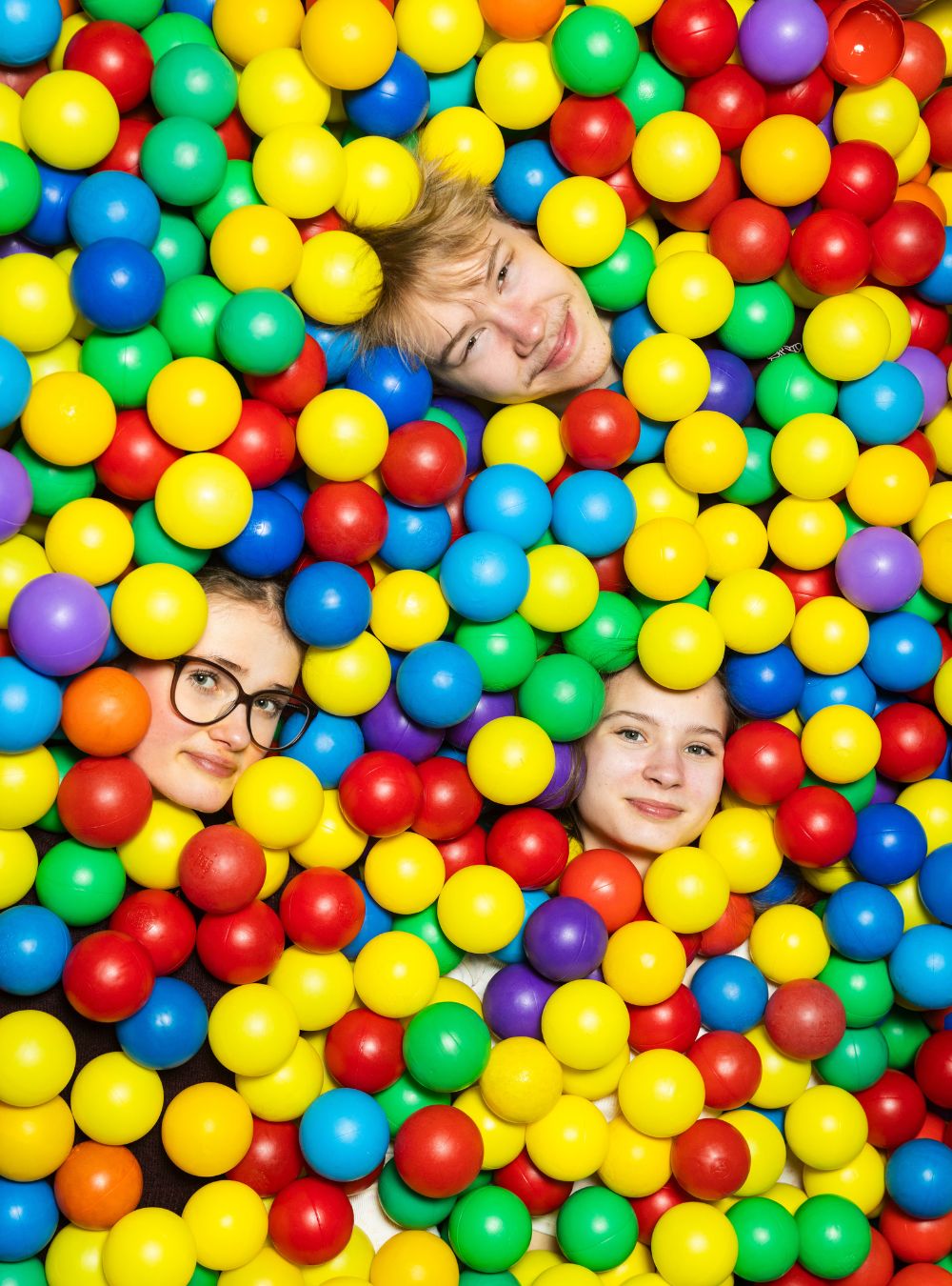 Kolme nuorta pallomeressä. Vain kasvot näkyvät pallojen keskeltä.