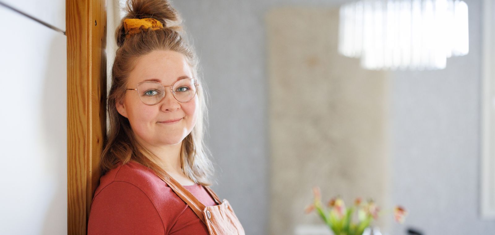 Eveliina Meriö nojaa ovenkarmiin, takana auringonvalossa kylpevä huone.