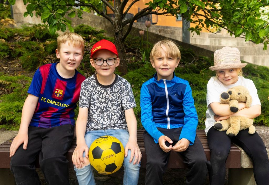 Neljä iltapäiväkerholaista istuu penkillä vierekkäin.